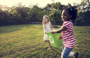 Kids running side by side with recycling bin between them
