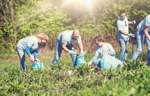 volunteering, charity, cleaning, people and ecology concept - group of happy volunteers with garbage bags cleaning area in park